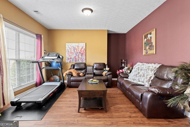 living room with wood finished floors, a textured ceiling, baseboards, and visible vents