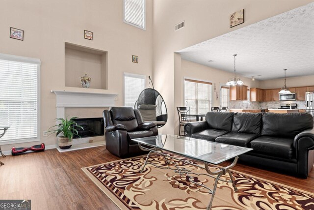 living area with a fireplace with raised hearth, baseboards, dark wood finished floors, visible vents, and a notable chandelier