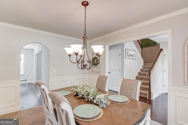 dining space featuring a wainscoted wall, crown molding, stairway, arched walkways, and a notable chandelier