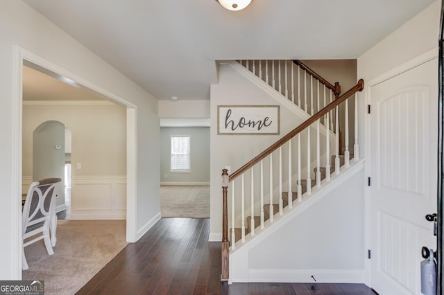 foyer with a wainscoted wall, stairway, a decorative wall, arched walkways, and dark wood-type flooring
