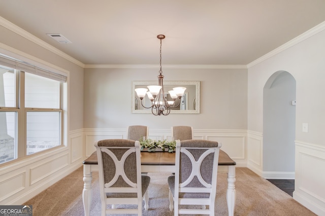 carpeted dining space with a chandelier, a wainscoted wall, arched walkways, visible vents, and a decorative wall