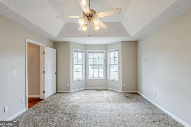 unfurnished bedroom with a textured ceiling, a tray ceiling, baseboards, and carpet