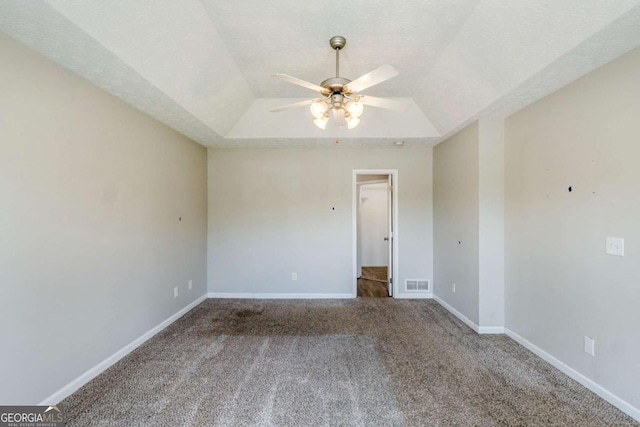 carpeted empty room with a textured ceiling, visible vents, baseboards, ceiling fan, and a raised ceiling