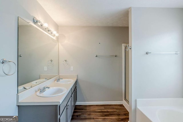 bathroom featuring baseboards, wood finished floors, a shower with door, a sink, and a garden tub