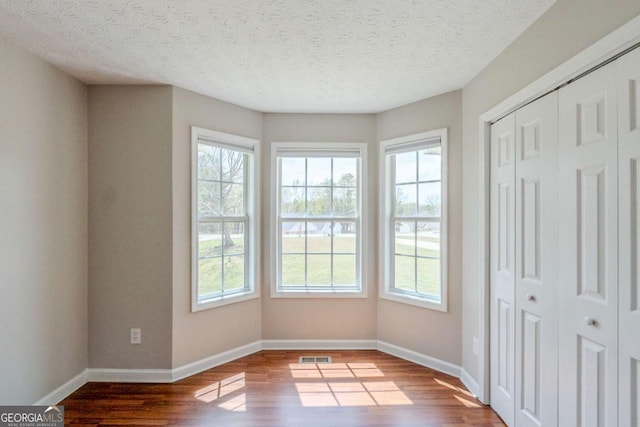 unfurnished bedroom with a closet, wood finished floors, a textured ceiling, baseboards, and visible vents