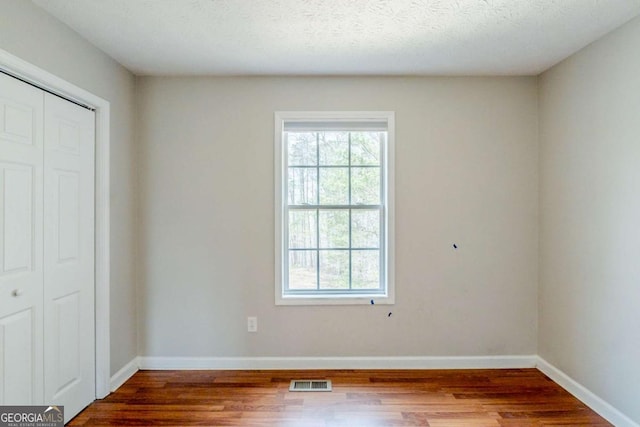 unfurnished bedroom with wood finished floors, baseboards, multiple windows, and visible vents