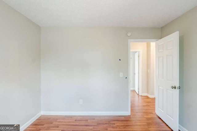 spare room featuring baseboards, light wood-type flooring, and a textured ceiling