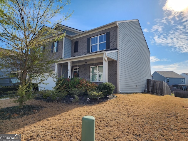 view of front of house with brick siding, a porch, fence, and a front lawn