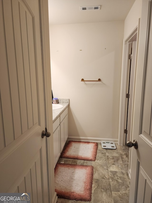 bathroom featuring stone finish flooring, vanity, visible vents, and baseboards