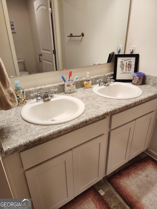 bathroom featuring toilet, double vanity, and a sink