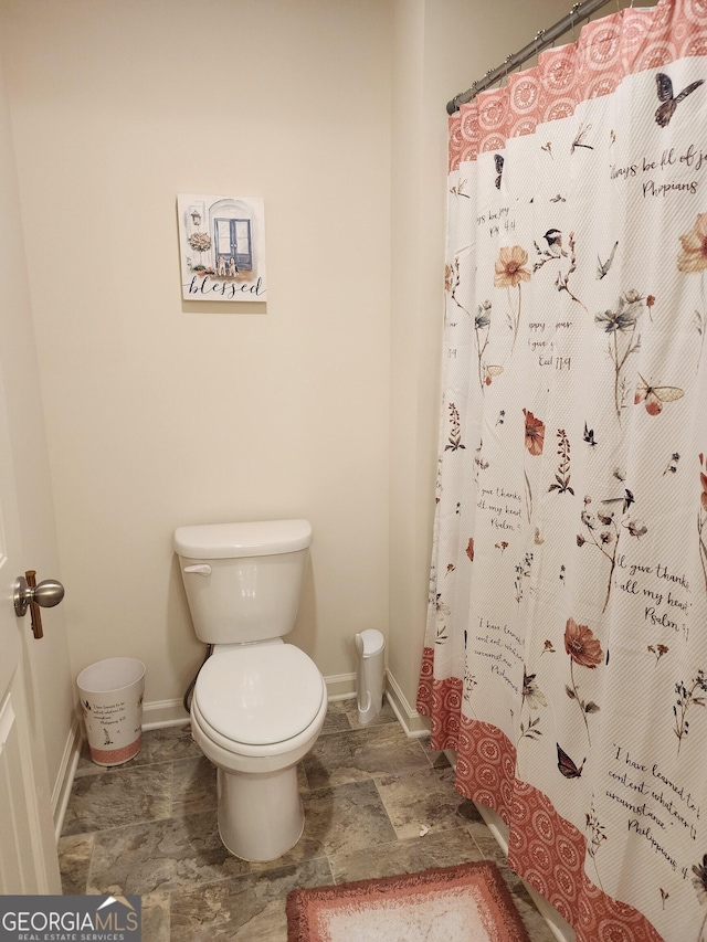 bathroom with toilet, stone finish floor, baseboards, and a shower with shower curtain