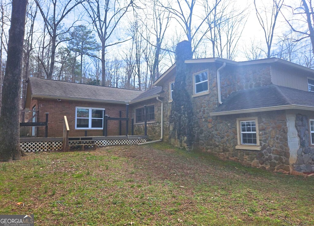 back of house with stone siding, a lawn, a deck, and a chimney