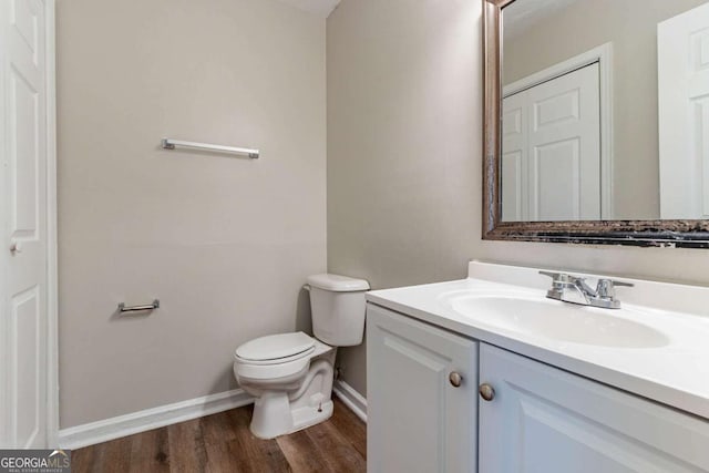half bathroom with toilet, vanity, baseboards, and wood finished floors