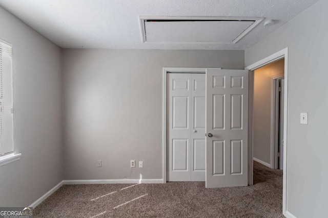 unfurnished bedroom with attic access, baseboards, a closet, and carpet