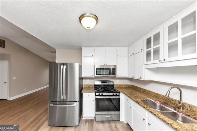 kitchen with light wood-type flooring, a textured ceiling, a sink, white cabinets, and appliances with stainless steel finishes