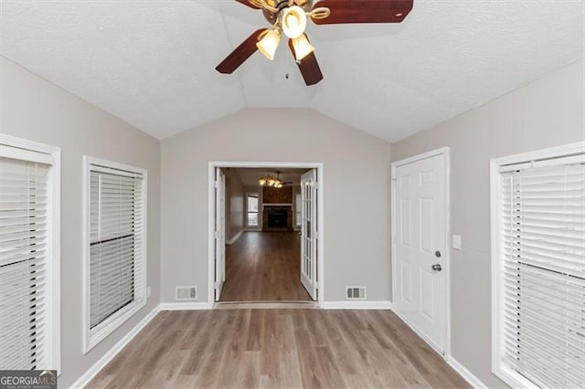 interior space featuring ceiling fan with notable chandelier, visible vents, light wood-style flooring, and vaulted ceiling