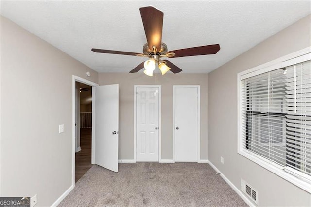 unfurnished bedroom with carpet flooring, baseboards, multiple closets, a textured ceiling, and visible vents