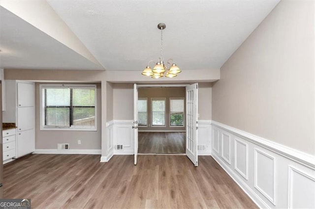 unfurnished dining area with a wealth of natural light, visible vents, light wood-style floors, and an inviting chandelier