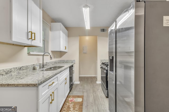 kitchen with white cabinets, gas stove, a sink, light wood-style floors, and visible vents