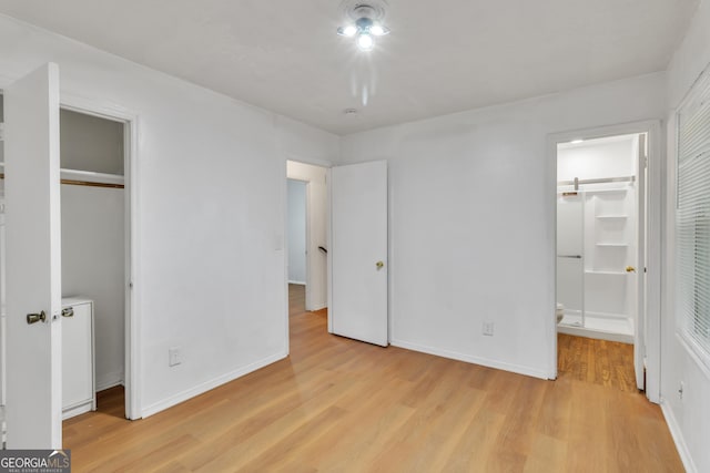 unfurnished bedroom featuring baseboards, light wood-style flooring, ensuite bathroom, and a closet