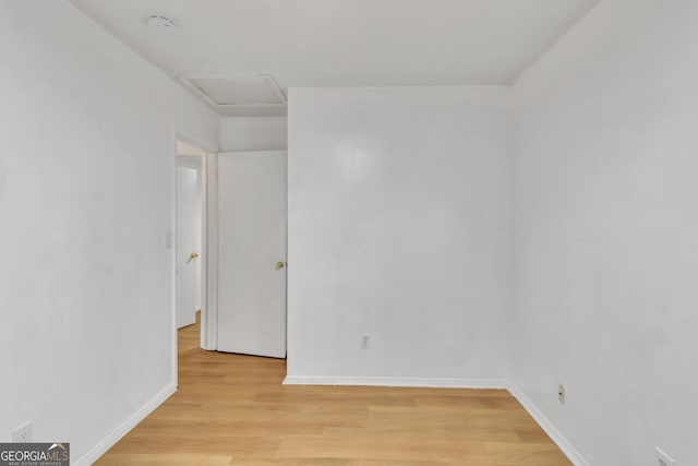 empty room with baseboards, attic access, and light wood finished floors
