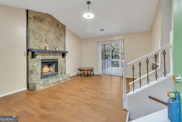 living area with visible vents, a fireplace, wood finished floors, baseboards, and lofted ceiling