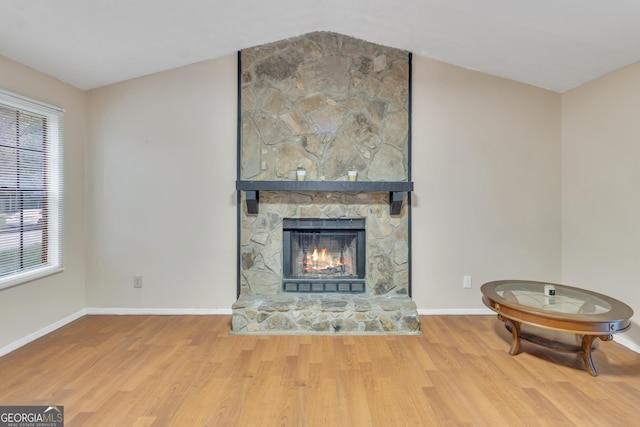 living area with baseboards, wood finished floors, vaulted ceiling, and a stone fireplace