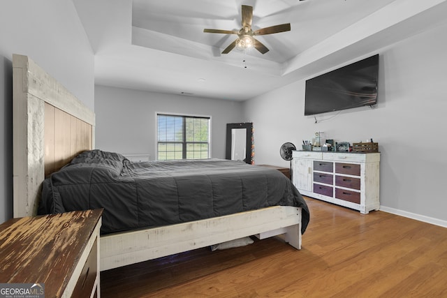 bedroom with ceiling fan, baseboards, wood finished floors, and a raised ceiling