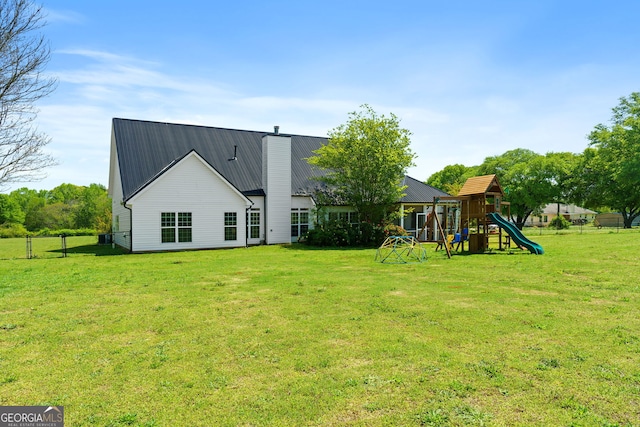 back of property featuring a chimney, metal roof, a playground, and a lawn