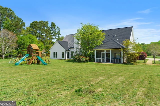 back of house with metal roof, a playground, a sunroom, and a lawn