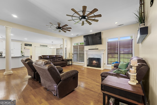 living area with a high end fireplace, ornate columns, ceiling fan with notable chandelier, and wood finished floors