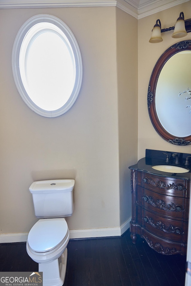 half bath with vanity, ornamental molding, wood finished floors, toilet, and baseboards