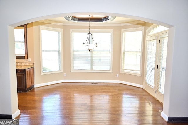 unfurnished dining area with crown molding, arched walkways, and hardwood / wood-style floors