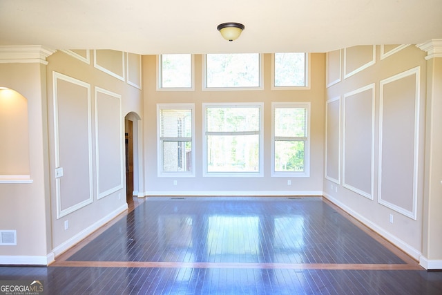 unfurnished living room featuring visible vents, arched walkways, baseboards, wood-type flooring, and a decorative wall