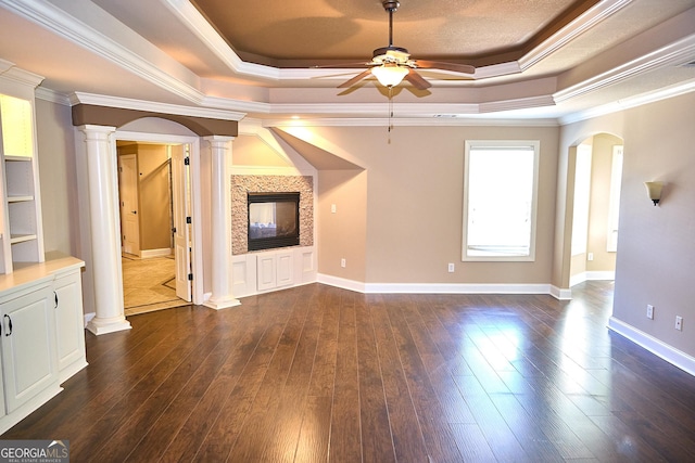 unfurnished living room featuring ceiling fan, decorative columns, arched walkways, a tray ceiling, and dark wood-type flooring