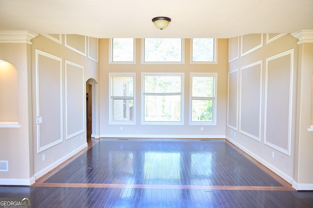 unfurnished living room with arched walkways, baseboards, a healthy amount of sunlight, and hardwood / wood-style flooring