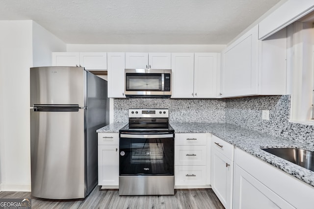 kitchen with light stone counters, light wood-type flooring, white cabinetry, and stainless steel appliances