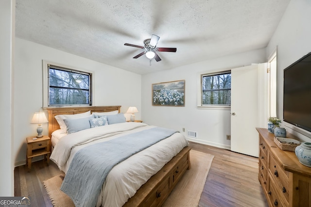 bedroom featuring wood finished floors, visible vents, a ceiling fan, baseboards, and a textured ceiling