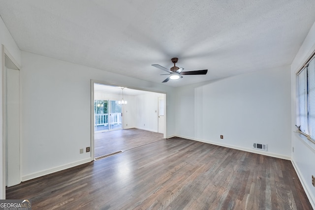 empty room with a textured ceiling, ceiling fan with notable chandelier, baseboards, dark wood-type flooring, and visible vents
