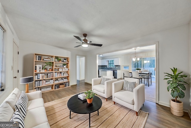 living area with ceiling fan with notable chandelier, baseboards, and wood finished floors