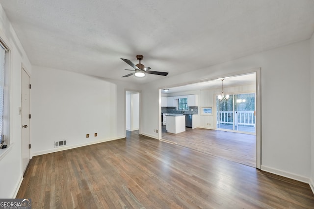 unfurnished living room with ceiling fan with notable chandelier, baseboards, dark wood-style floors, and visible vents