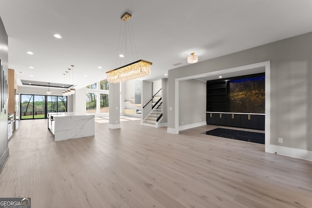 unfurnished living room with light wood finished floors, baseboards, a chandelier, and recessed lighting