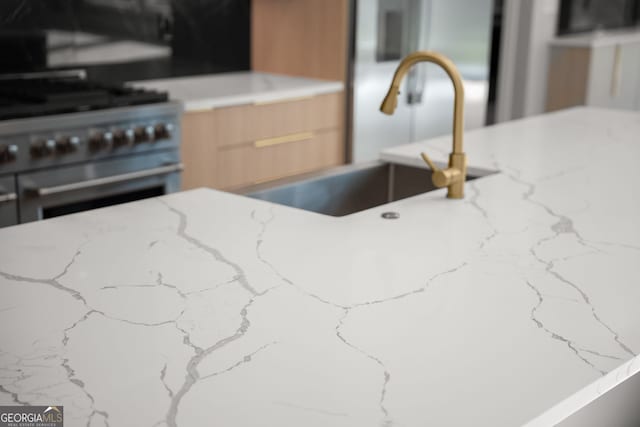 interior details with stainless steel gas range, modern cabinets, a sink, and light stone counters