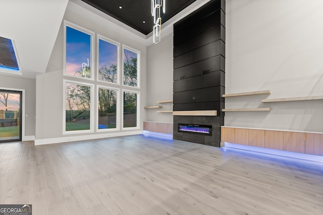 unfurnished living room with a high ceiling, plenty of natural light, a large fireplace, and light wood-style floors