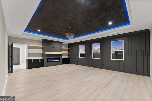 unfurnished living room featuring a tray ceiling, baseboards, light wood finished floors, and a large fireplace