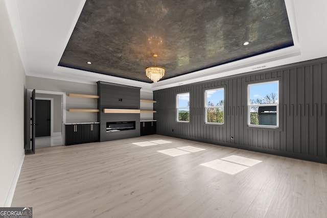 unfurnished living room featuring a large fireplace, crown molding, light wood finished floors, baseboards, and a tray ceiling