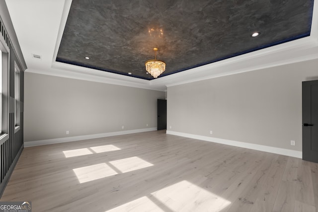 unfurnished room featuring an inviting chandelier, ornamental molding, baseboards, a raised ceiling, and wood finished floors