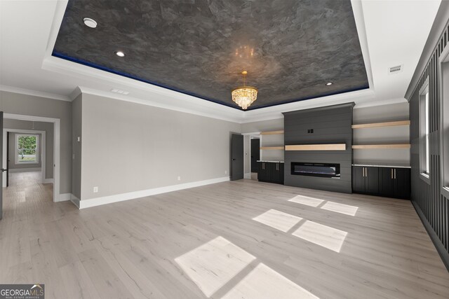 unfurnished living room featuring a raised ceiling, crown molding, light wood-style floors, and baseboards
