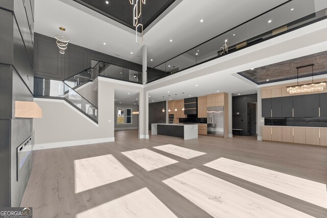 interior space with light wood-style flooring, a chandelier, baseboards, a towering ceiling, and stairway
