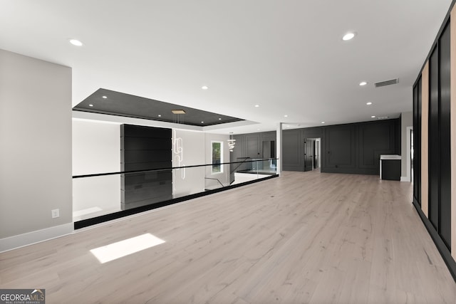 unfurnished living room with light wood-style flooring, visible vents, baseboards, recessed lighting, and a tray ceiling